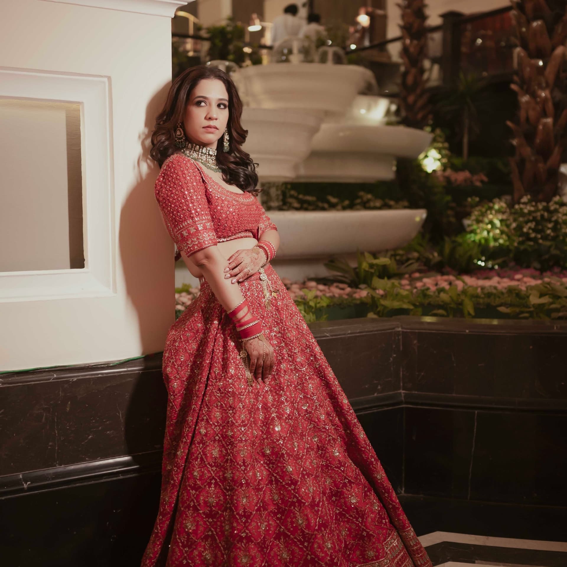 A bride in a red lehenga beside a fountain at night