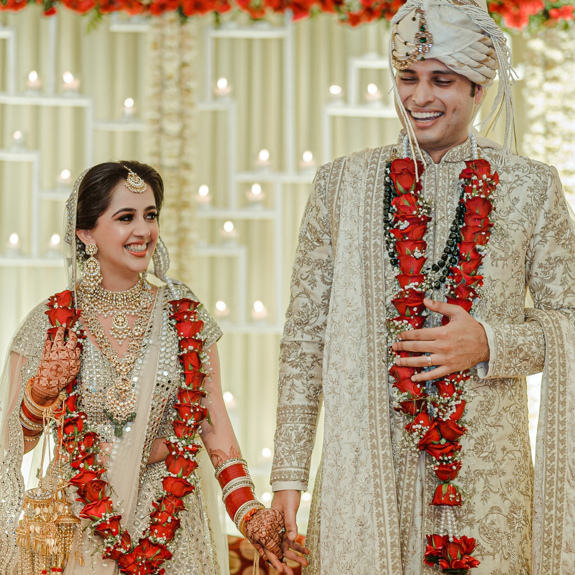 A couple holding hands beneath red floral garlands