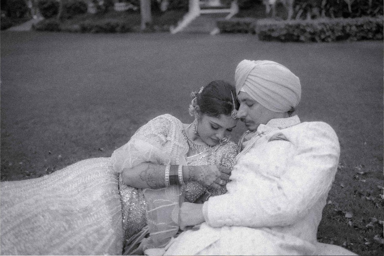 A bride resting against the groom as they sit together on the lawn