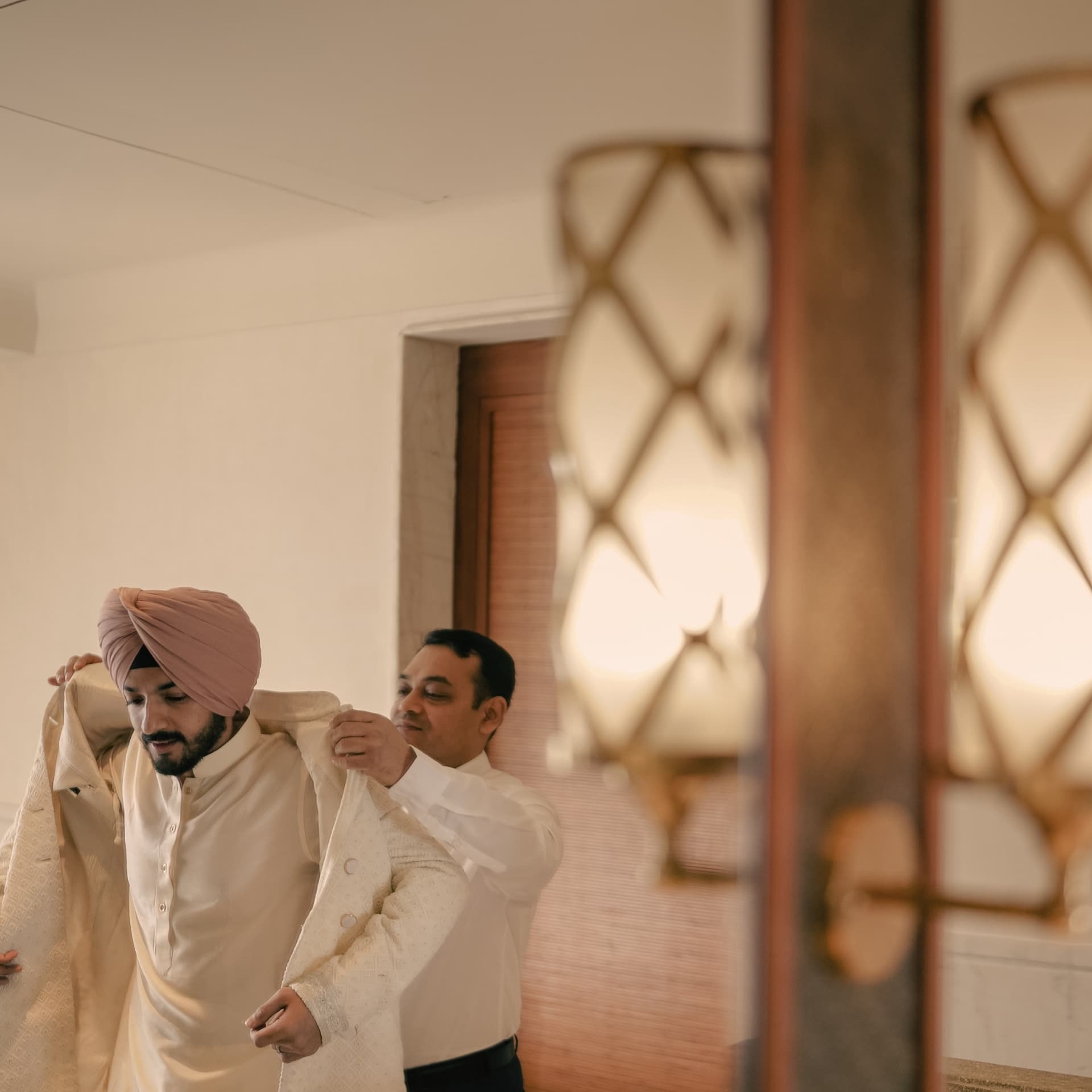 A groom helped into his sherwani by lamplight
