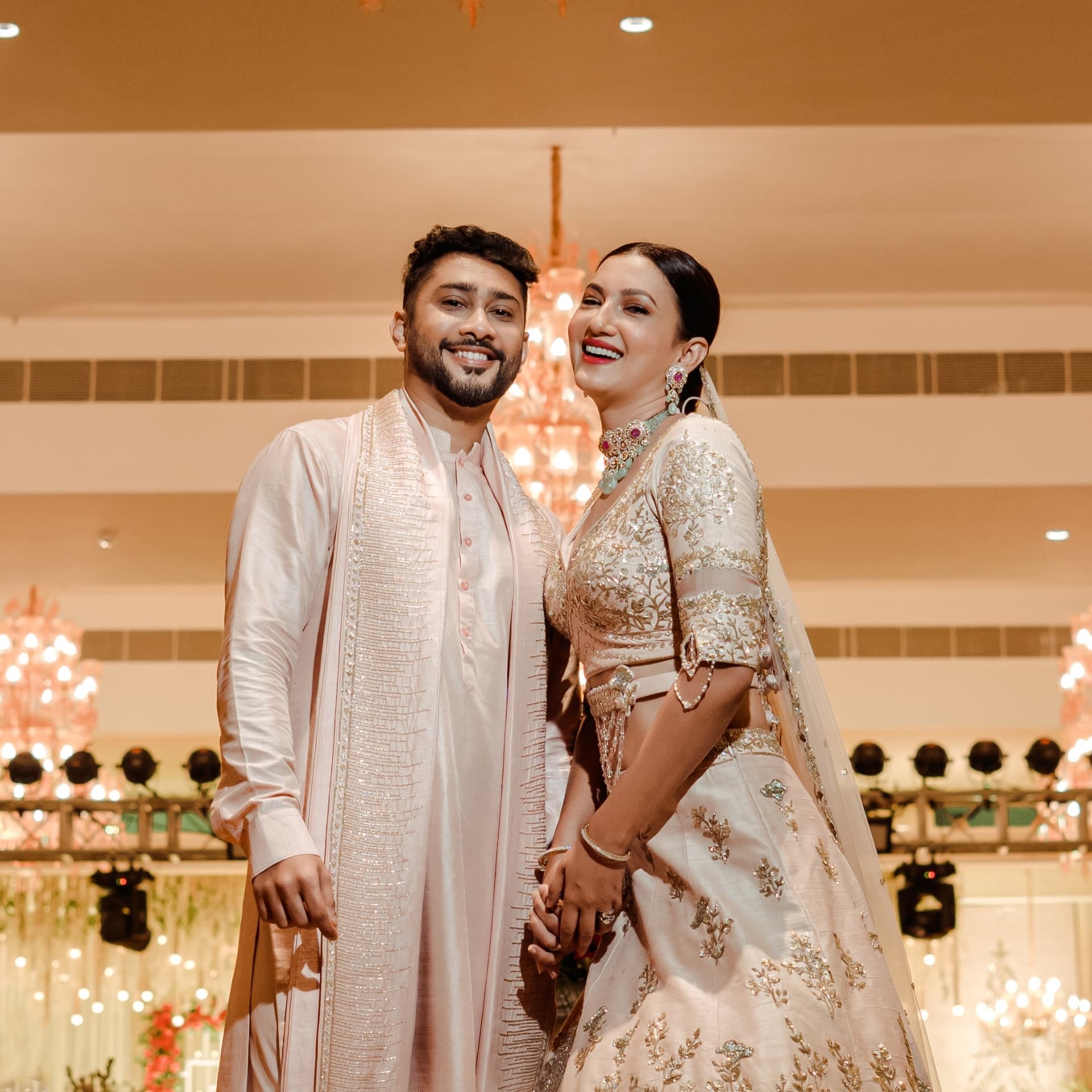 A couple in blush attire beneath chandeliers