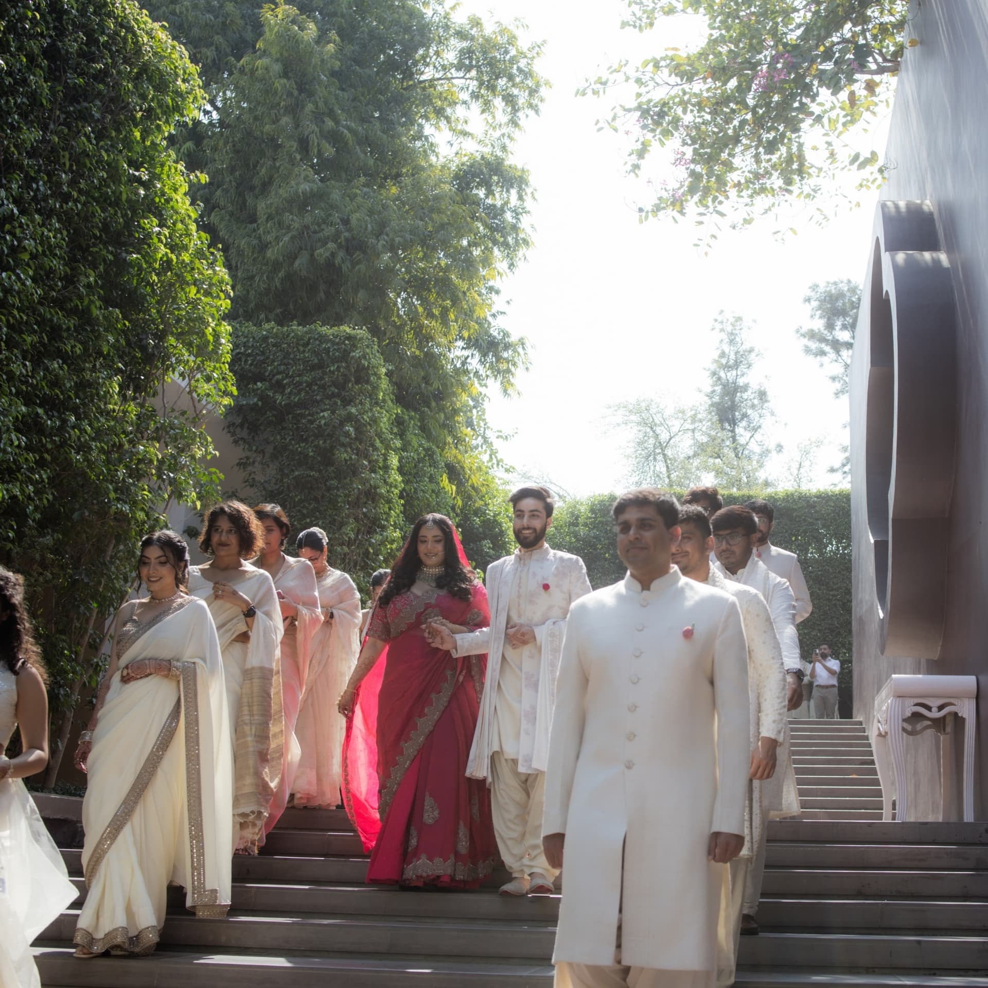 The wedding party descending garden steps in cream and crimson